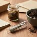 Close-up of THCA pre-roll tube, rolling papers, and compostable plant material on a wooden table with a compost bowl and recycling-friendly materials in the background.