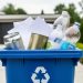 Close-up of a recycling bin filled with an aluminum can, steel can, paper, and plastic bottles in a residential setting.